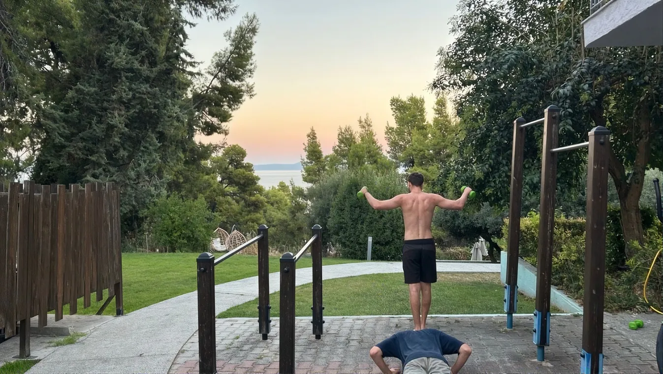 A friend doing a handstand on the parallel bars in a park at sunset.