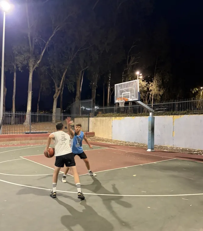 Two friends playing basketball on an outdoor court at night.